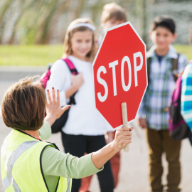 school crossing guard holding a stop sign with schoolchildren in the background